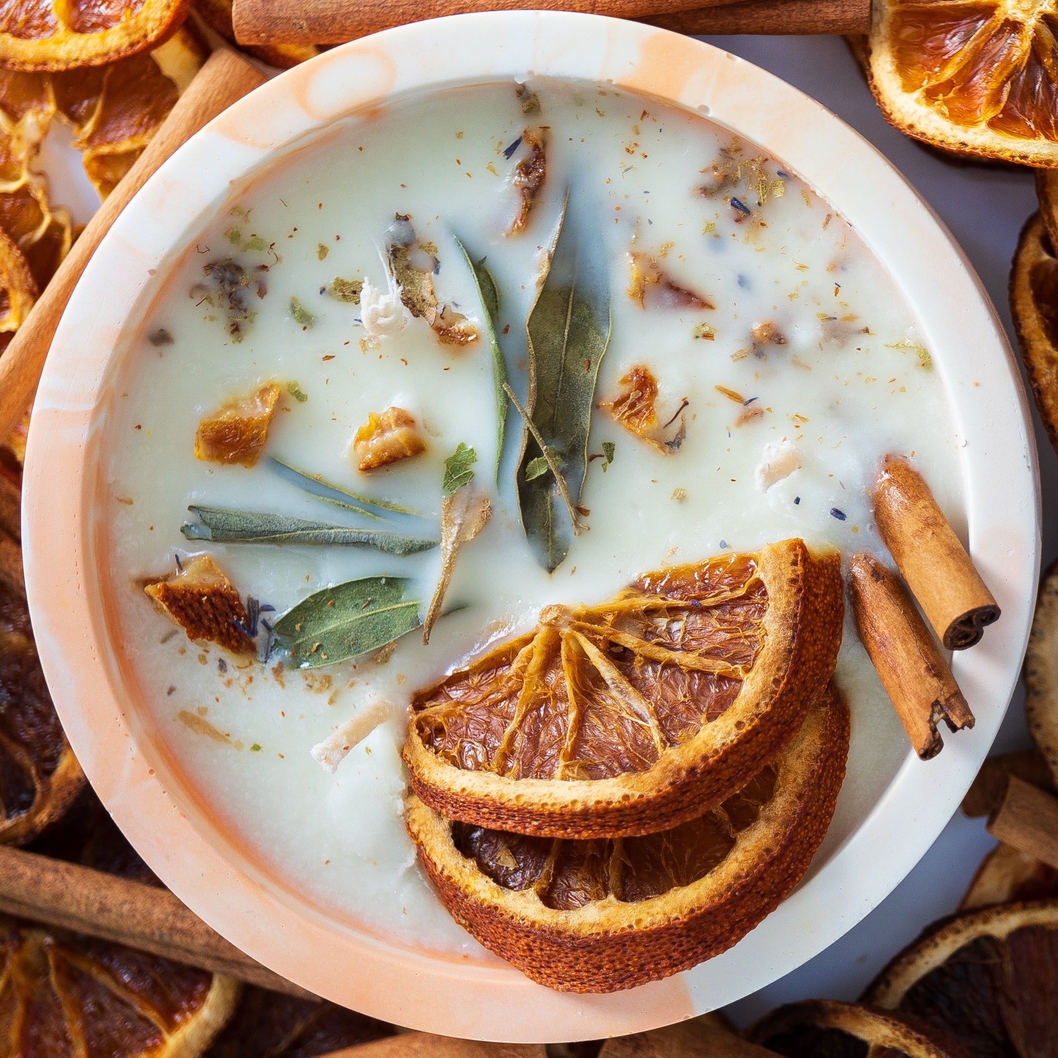 Dried oranges, cinnamon sticks, and a bowl of cream on a white surface