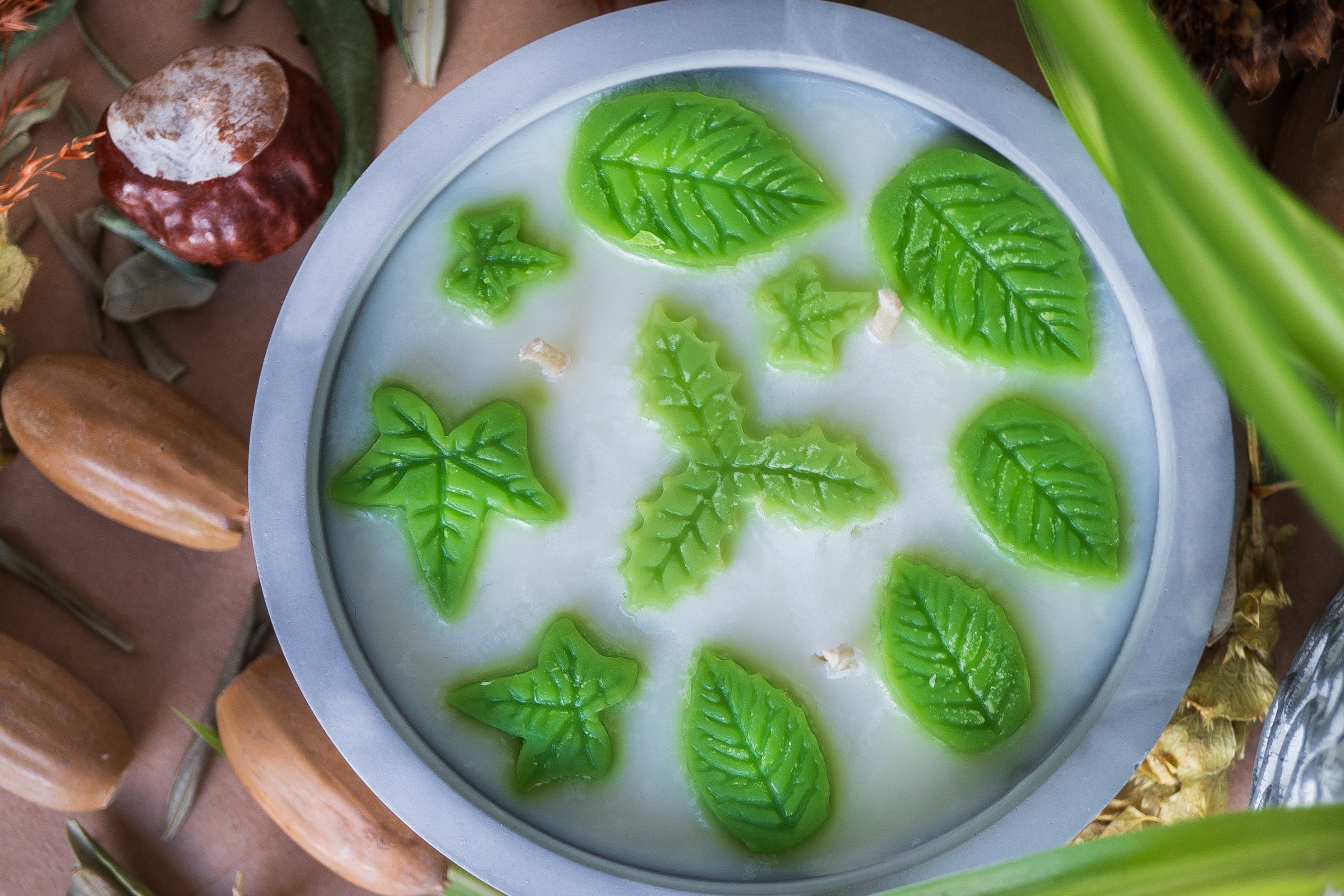 Candle with green leaf-shaped wicks on a decorative surface