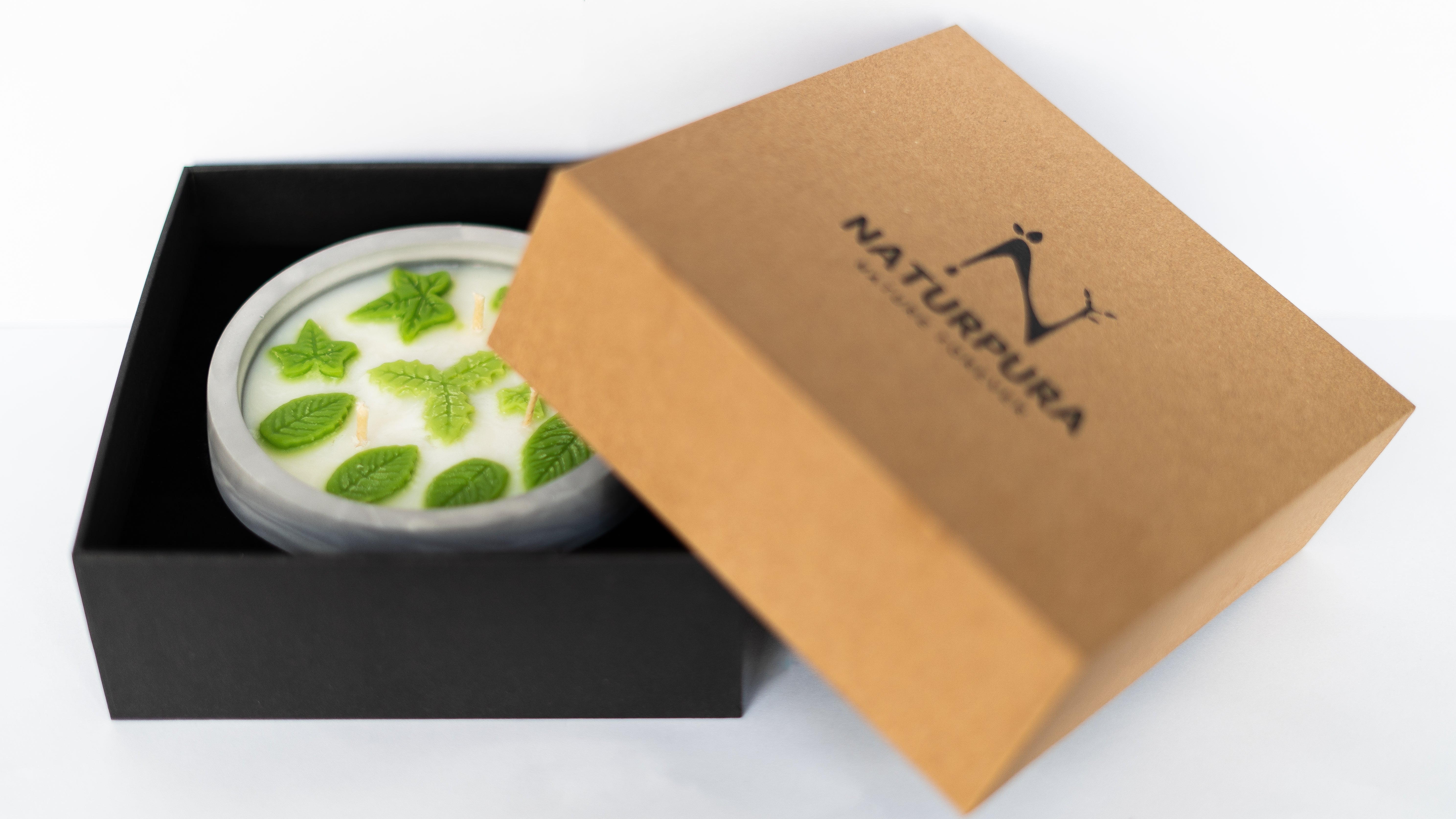 Candle in a gray holder with green wax and wicks, surrounded by plants and natural elements.