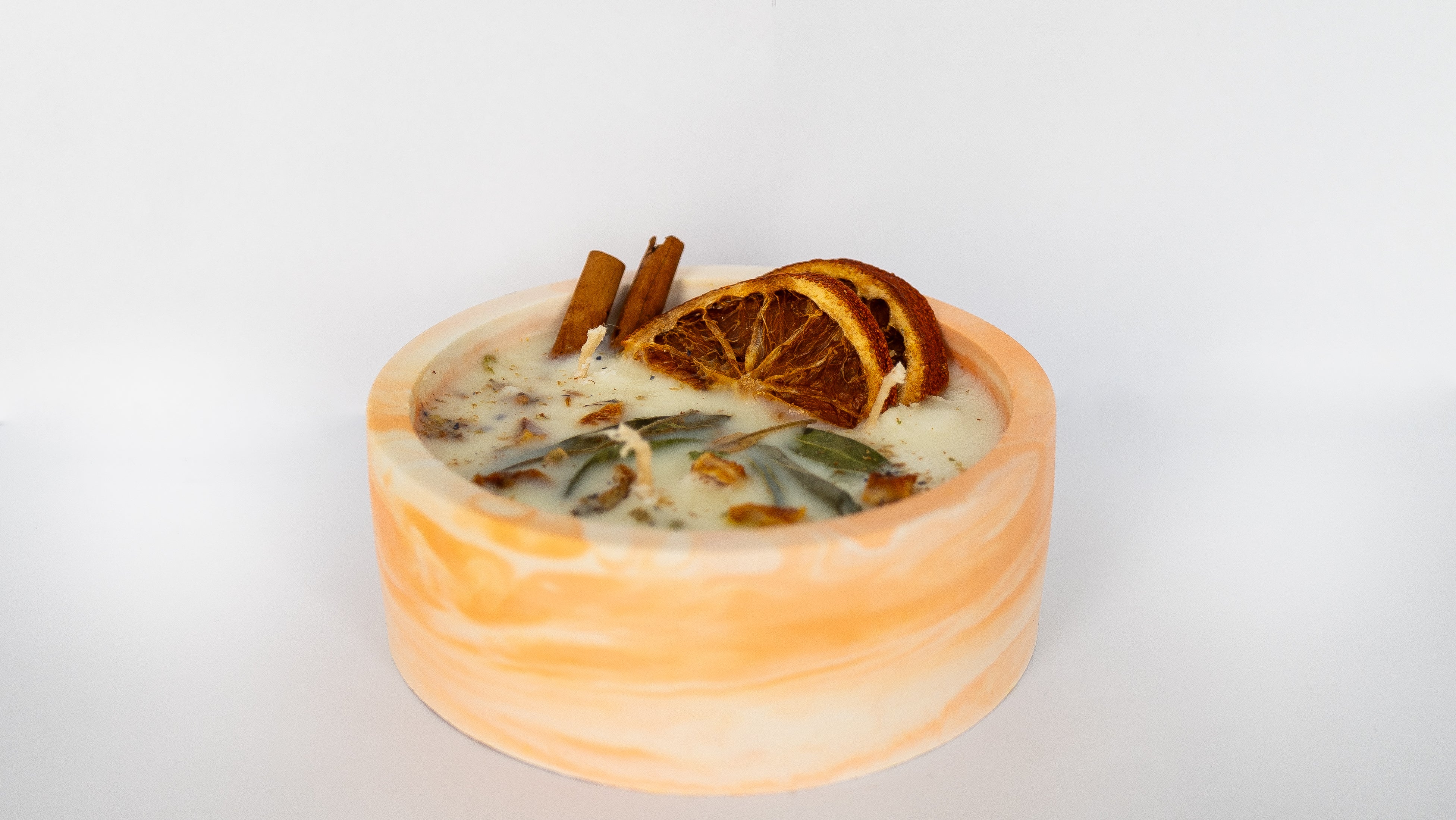 Dried oranges, cinnamon sticks, and a bowl of cream on a white surface